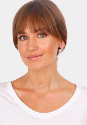Gold choker necklace with a crescent moon pendant and small circular accent. Worn over a white shirt, highlighting the delicate design.