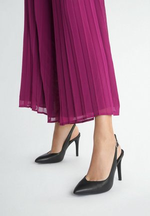 Tacchi alti neri con cinturino alla caviglia, punta affusolata, materiale in pelle liscia, tacco sottile e alto, posti su un vestito magenta plissettato.