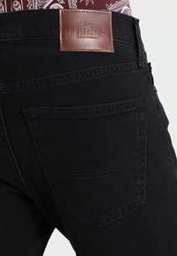 Czarne dżinsy z denimu z skórzaną naszywką oznaczoną "HOLLISTER CALIFORNIA", z dwoma tylnymi kieszeniami i subtelnymi detalami w szwach.