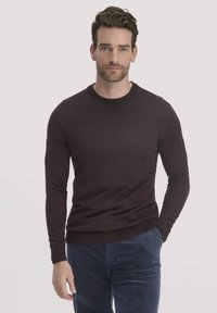 Dunkellila, langärmliger Rundhals-Pullover aus einem glatten Stoff, enganliegendes Design mit gerippten Bündchen und Saum, kombiniert mit strukturierten blauen Cordhosen.