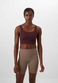 Bordó cropped tank top és világosbarna, magas derekú short. Mindkettő sima, rugalmas anyagból készült, minimális varrásokkal és testhezálló kialakítással.
