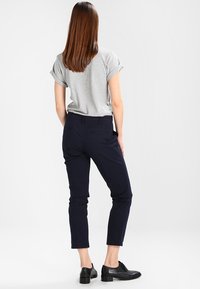 Grå t-shirt med rullade ärmar i kombination med marinblå slim-fit byxor. Byxorna har två bakfickor och en kortad design. Svarta skor fulländar outfiten.