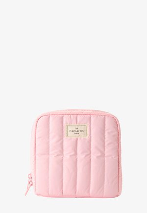 Bolsa de cosméticos cuadrada acolchada de color rosa claro con costuras verticales y una pequeña etiqueta en la parte frontal que dice "The Flat Lay Co. London".