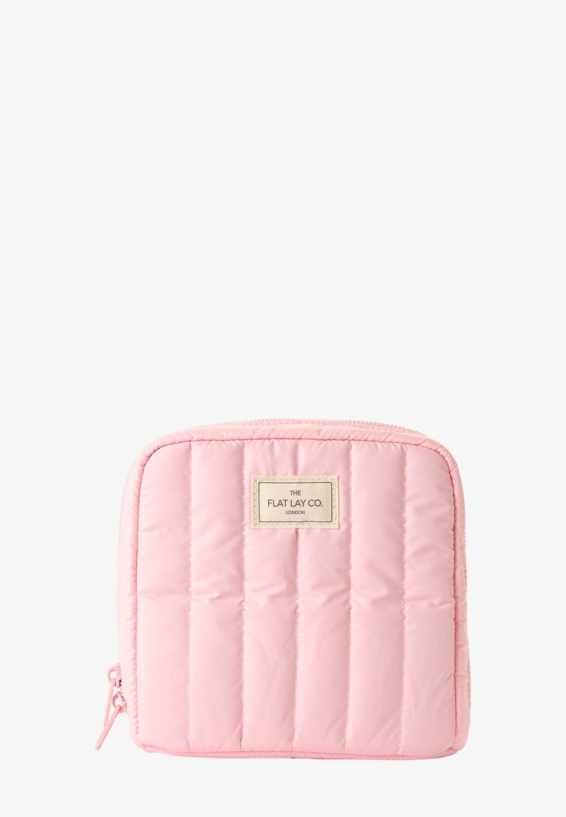 Trousse cosmétique carrée matelassée rose clair avec des coutures verticales et une petite étiquette portant l'inscription "The Flat Lay Co. London" à l'avant.
