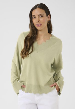 Pull vert clair avec un col en feston et un ourlet irrégulier, manches longues et coupe décontractée. Réalisé en matière tricotée douce et texturée.