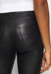 Pantaloni in pelle nera con vestibilità slim, dotati di tasche posteriori curve e dettagli di cucitura sottili. Texture morbida con una finitura elegante.