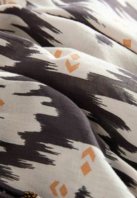 Tissu avec un motif abstrait de coups de pinceau en noir et blanc, accentué par de petites formes géométriques orange, montrant des plis doux et une texture.