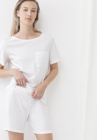 Witte katoenen t-shirt met een ronde halslijn en een zak; gecombineerd met witte katoenen shorts met een elastische tailleband. Eenvoudig en onopvallend ontwerp.
