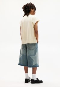 Korte mouw beige t-shirt, lichtblauwe denim culottes met sterrenpatronen, zwarte schoenen en witte sokken. Achteraanzicht.