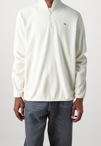 Pullover in pile bianco con collo a mezza zip, maniche lunghe e fondo elasticizzato. Presenta un piccolo logo sul petto sinistro.