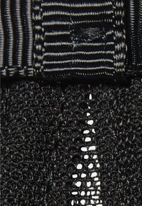 Tejido negro texturizado con un intrincado patrón de tejido abierto, complementado por un diseño a rayas en el borde.