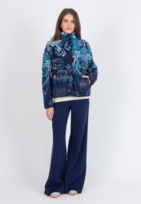 Zils rakstains džemperis ar žaketi, augstu apkakli un pogu aizdari. Gluda tekstūra, veidota ar zilo, baltu un tumši zilo toņu kombināciju.