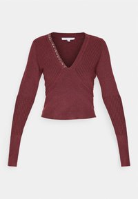 Haut en maille bordeaux profond à manches longues avec col en V, manches côtelées, motif côtelé diagonal et détails en œillets métalliques le long d'un côté de l'encolure.