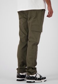 Olijfgroene cargobroek van stof, met zijzakken, een normale pasvorm en omgeslagen broekspijpen, gecombineerd met zwart-witte sneakers met een patroon.