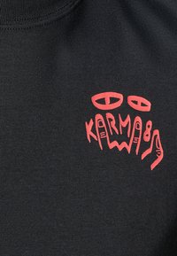 Black T-shirt with a prominent red graphic reading "KARMA." Design includes abstract eyes and stylized letters. Cotton fabric, short sleeves.
