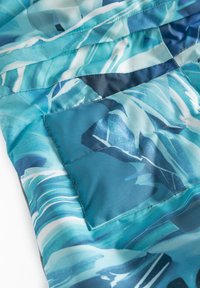 Tejido en tonos azules y verde azulado con patrones de olas abstractos. Presenta una textura suave y un detalle de bolsillo cosido.