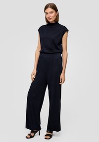 Marineblauwe geribde jumpsuit met korte mouwen, hoge hals en wijde pijpen. Draag het met zwarte hoge hakken. Eenvoudig en elegant ontwerp.