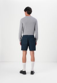 Gray long-sleeve shirt, navy shorts with a textured pattern, two back pockets, worn with white socks and black loafers. Standing position.