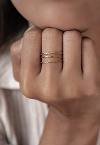 Tre anelli d'oro con motivi testurizzati diversi, inclusi un design attorcigliato, impilati su una mano con tonalità della pelle sottili.