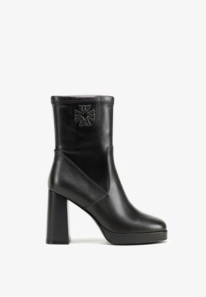 Černá kožená kotníková bota s blokovým podpatkem, s kulatou špičkou a dekorativním prošíváním. Na přední části je viditelný reliéfní křížový vzor.