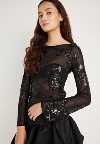 Top preto de malha com mangas compridas, decorado com padrões florais bordados e lantejoulas, combinado com uma saia preta volumosa de cetim.