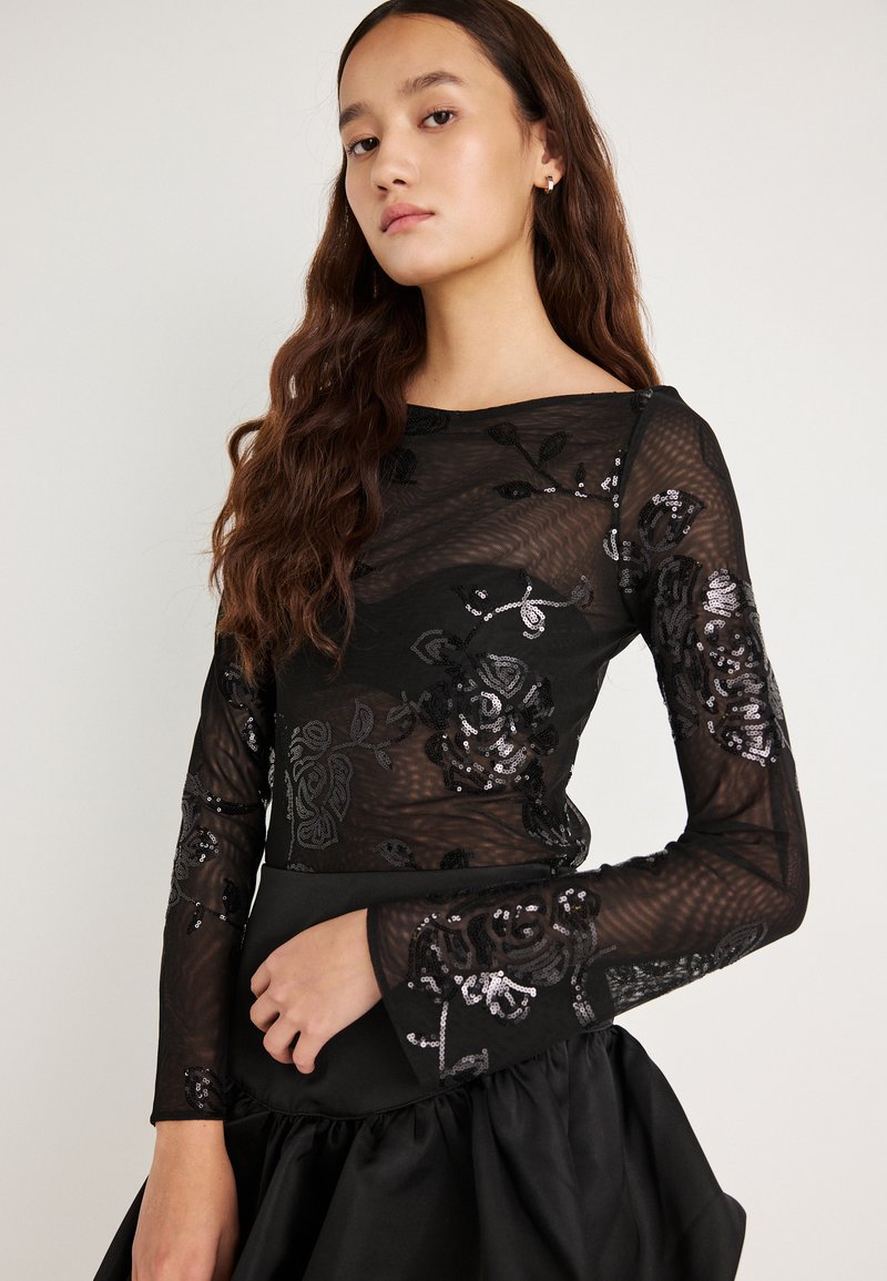 Top preto de malha com mangas compridas, decorado com padrões florais bordados e lantejoulas, combinado com uma saia preta volumosa de cetim.