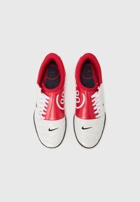 Des chaussures de sport rouges et blanches avec une tige lisse, un logo Nike noir, des lacets blancs et un intérieur rembourré rouge. Présente une section de orteil texturée blanche.