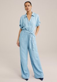 Lyseblå, bælteholdt jumpsuit med kravehals, korte ærmer og vidde ben, lavet af et blødt, flydende stof.