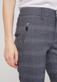 Navy geblokte broeken hebben een gestructureerde stof, een slim fit, zichtbare zijrits zakken en contrasterende stikseldetails.