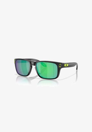 Occhiali da sole neri con montature angolari, dotati di lenti a gradiente verde. Accentuati da piccole macchie gialle sulle tempie. Finitura liscia.