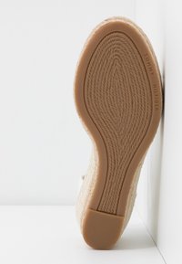 Semelle de chaussure compensée espadrille beige avec motif en corde texturée et talon en caoutchouc, marqué de la marque "Tommy Hilfiger" sur le côté.