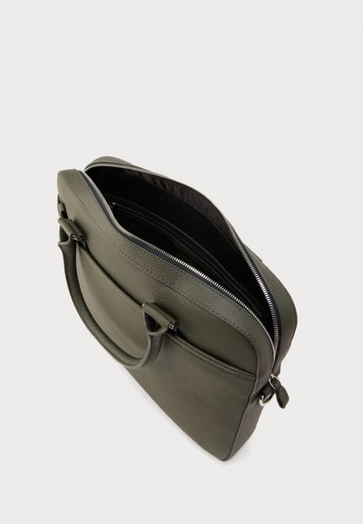 Χακί δερμάτινη τσάντα με λεία υφή, κλείσιμο με φερμουάρ, δύο λαβές και εξωτερική τσέπη. Το εσωτερικό περιλαμβάνει πολλαπλά διαμερίσματα.