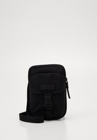 Borsa a tracolla in nylon nero con chiusura a zip, pattina frontale, tracolla e etichetta testurizzata. Forma rettangolare compatta con hardware minimale.