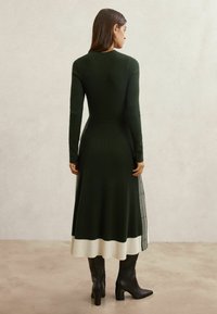 Robe en maille côtelée verte avec manches longues, corsage ajusté et ourlet évasé avec un bas contrastant blanc et côtelé.