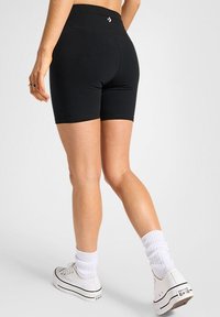 Pantalones cortos ajustados negros con una cinturilla alta, hechos de material elástico, combinados con calcetines tobilleros blancos y zapatillas casuales blancas.