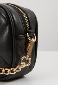Borsa a tracolla in pelle nera con design trapuntato, chiusura e accessori dorati. Presenta una tracolla in catena dorata e una superficie testurizzata.
