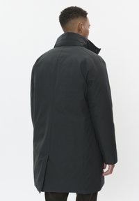 Tumši pelēkā mētelis ar augstu apkakli, ar elegantu dizainu, taisnu griezumu un vieglu spraugu aizmugurē. Gluda tekstūra.