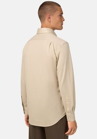 Camicia beige a maniche lunghe con colletto classico, polsi abbottonati e orlo curvo, realizzata in tessuto morbido con una leggera lucentezza.