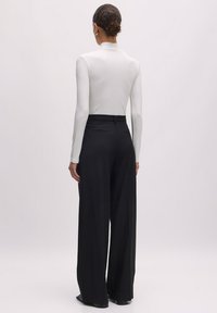 Witte geribbelde lange mouwtop gecombineerd met hoge zwarte wijde broek, met een gladde textuur en zonder zichtbare patronen of hardware.