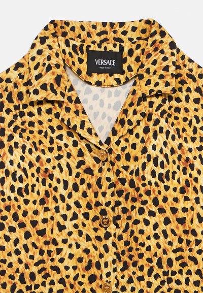 Košulja s leopard uzorkom koja ima ovratnik, zlatne gumbe i tkaninu koja izgleda glatko. Oznaka marke vidljiva je na rubu vrata.