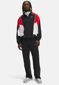 Sports tracksuit med et sort, rødt og hvidt farveblokdesign. Jakken har en kvart lynlås og bukserne har hvide sidelister.
