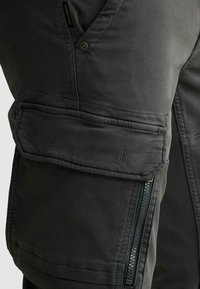 Close-up van zak van cargobroek van donker stof met klep, knoop en verticale ritssluitingsdetail.