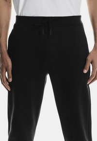 Zwarte joggerbroeken met een gladde textuur en een elastische tailleband met een trekkoord. Zijzakken voegen functionaliteit toe aan het ontwerp.