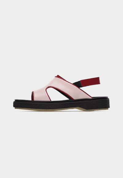 Sandale à bouts ouverts avec empeigne rose clair, semelle noire et sangle arrière réglable rouge, présentée sur un fond uni.