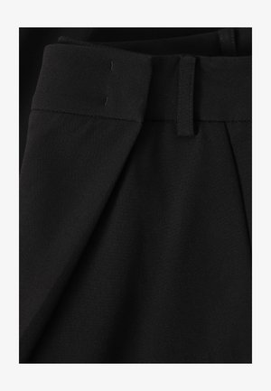 Zwarte op maat gemaakte broek met riemlussen en geplooide voorkant, close-up van de tailleband en het bovenste stofdetail.