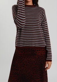 Maglione a righe marrone e grigio con maniche lunghe e scollatura rotonda, abbinato a una gonna bordeaux con stampa leopardata.
