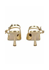 Een paar gouden sandalen met hoge hakken en bandjes bij de enkels, gezien van achteren op een witte achtergrond.