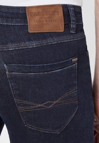 Donkerblauwe denim jeans met een leren label met de tekst "Paddock's." Voorzien van oranje stiksels en een achterzak met een gebogen ontwerp.