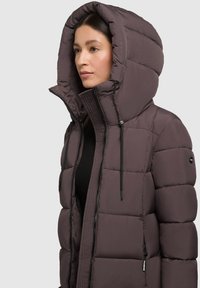 Podložena kapuća jakna v temno vijolični barvi, ki ima zadrgo na sprednji strani, nastavljive vrvi in teksturiran notranji panel. Gladek, vodoodporen material.