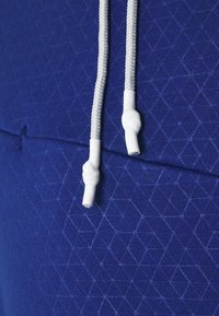 Blå sweatshirt i tyg med geometriskt mönster. Har vita dragsnören med texturerade toppar för säker justering.